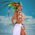 Mujer en atuendo polinésico con tocado de hojas y flores, topless, posando en una playa soleada.