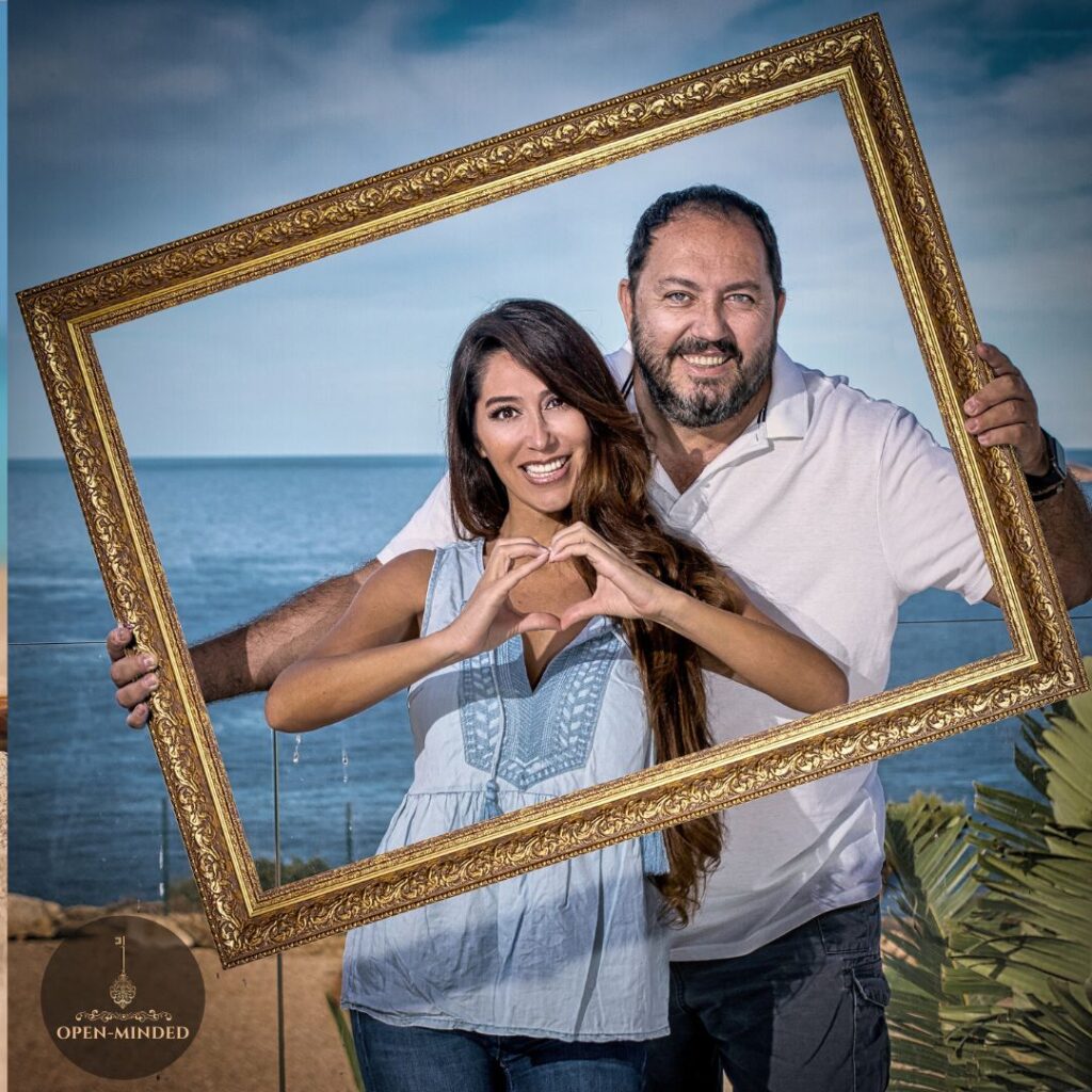 Pareja sonriente enmarcada frente al mar representando la autenticidad y el respeto en Open-Minded.club, el único club swinger auténtico en Valencia.